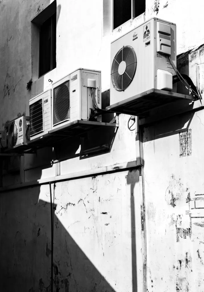 "Outdoor AC condenser units mounted on a building wall, showing the need for AC cleaning, HVAC ducting maintenance, and clean air duct services.